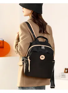 Detail of a lightweight black oxford backpack with an M-logo patch and dual zippers