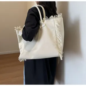 Détail du grand sac cabas en toile crème montrant les bords à franges et la texture