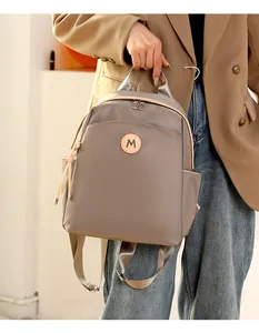 Detail of dark brown oxford backpack showing round M logo and silver metallic zippers