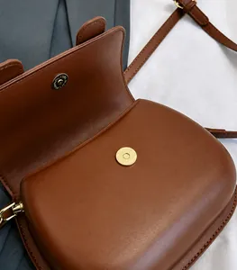 Detail of the golden magnetic buckle closure on a brown leather crossbody bag
