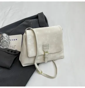 Close-up of cream messenger bag with marble texture and metal buckle on grey suit