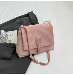 Close-up of pink frosted suede messenger bag with gold buckle on grey fabric