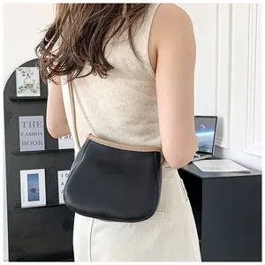 Vue latérale du sac selle en cuir grainé noir et beige porté par un mannequin