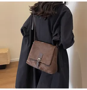 Detail view of a vintage brown messenger bag showing the textured matte leather and metal buckle