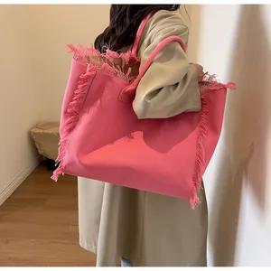 Détail du cabas en toile rose avec franges et bandoulière sur un manteau beige