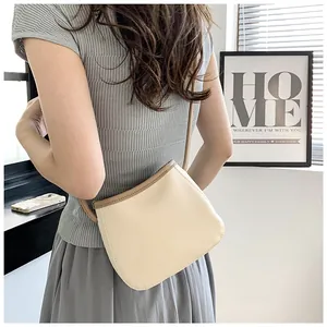 Détail du sac seau beige avec bordure marron montrant le grain de cuir et la bandoulière fine