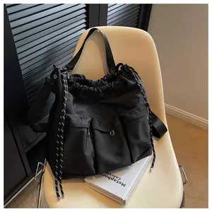 Detail of black nylon drawstring tote bag with triple front pockets on a wooden chair