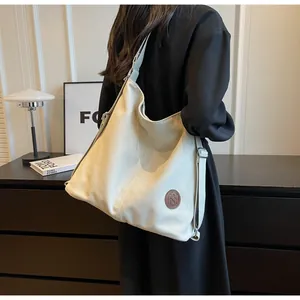 Detail of minimalist cream tote bag showing adjustable wide strap and round leather logo