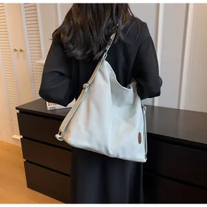 Detail of grey suede hobo bag with round leather logo and wide adjustable strap on model