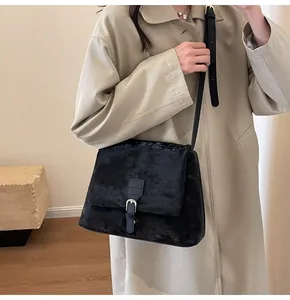 Close-up of black velvet crossbody bag with metal buckle on a beige trench coat