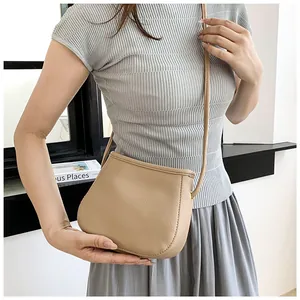 Gros plan du sac besace beige en cuir grainé avec finitions dorées et surpiqûres