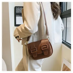 Detailed view of a brown leather crossbody square bag with gold hardware on a model