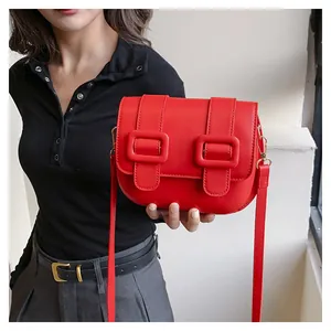 Detail shot of a red PU leather crossbody bag featuring dual large decorative square buckles