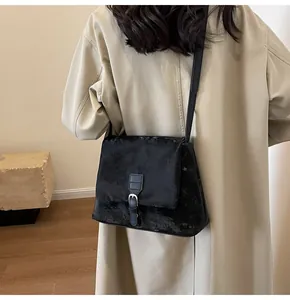 Detail of a vintage black messenger bag on a beige trench coat showing its matte texture