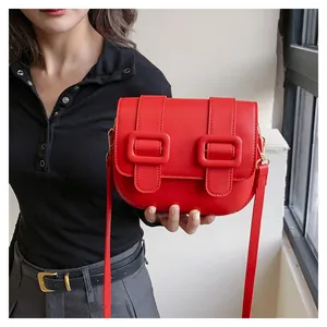 Close-up of a vibrant red saddle shoulder bag with dual square buckles and golden hooks