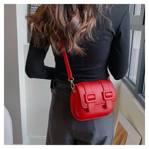 Detail view of red leather crossbody bag with double buckles worn by a model