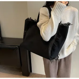 Détail du sac cabas en toile noire montrant les franges faites main et la texture