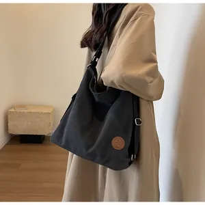 Detail view of black canvas tote bag showing side metal buckle and leather logo patch