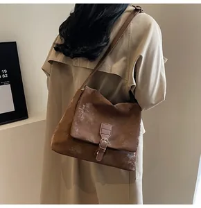 Close-up of a vintage brown messenger bag worn by a model against a minimalist wall