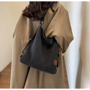 Detail shot of a black canvas tote bag with a brown leather logo patch on a khaki trench coat