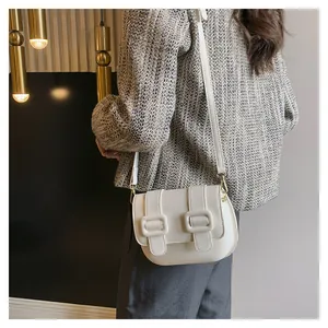 Detailed shot of off-white crossbody bag with dual decorative square buckles and gold hooks