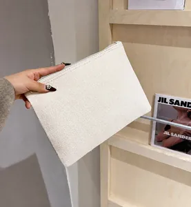 Detalle de un bolso de mano de lino crema con textura tejida y cremallera metálica