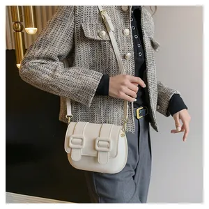Detail of a creamy white half-moon crossbody bag with double square buckles on matte leather