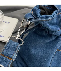 Macro detail of blue denim handbag featuring silver metal hooks and orange stitching