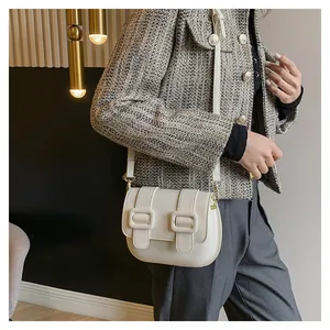 Chic cream-colored leather saddle bag with square buckles worn by a model in a luxury room