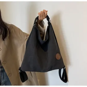 Close-up of black canvas tote bag with brown leather logo patch and wide strap