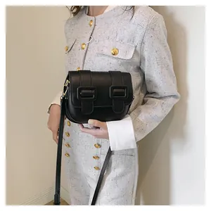 Detail of a black leather crossbody bag with double square buckles on a model
