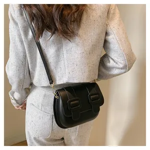 Side view of model wearing black crossbody bag with dual square buckles on beige tweed coat