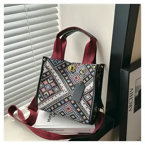 Detail of geometric woven tote bag with metallic twist lock and red carry handles