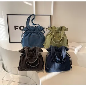 Detail of four colorful washed denim drawstring handbags with dual handles in a minimalist setting