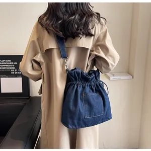 Close-up of a dark blue denim drawstring bucket bag with decorative pockets and topstitching