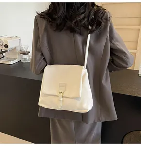 Close-up of creamy white leather messenger bag with flap and metal buckle detail