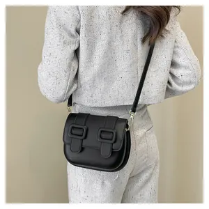 Detail of a black saddle crossbody bag with gold buckles worn as a stylish shoulder bag