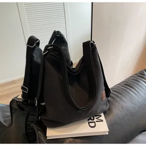 Detail of black canvas tote bag on leather sofa with side logo and wide strap