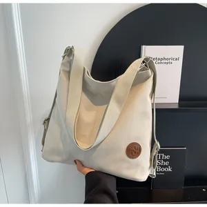 Detail of off-white canvas tote bag featuring brown leather logo and adjustable strap