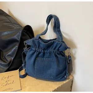 Detailed view of the drawstring closure and front pocket on this blue denim tote bag