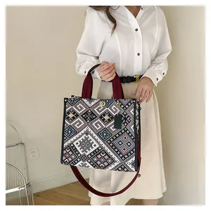Detailed close-up of woven ethnic pattern tote bag with gold lock and red handles