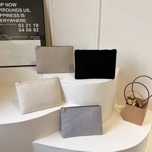 Détail de quatre pochettes en lin avec fermetures éclair dorées sur présentoir blanc