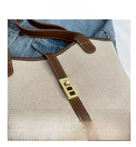 Detailed close-up of beige canvas tote with brown leather trim and gold swivel lock