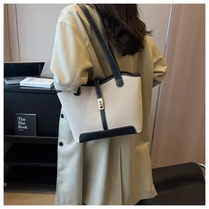 Detail of beige canvas tote with black leather trim and gold metal clasp on model