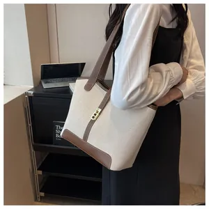 Detailed close-up of canvas tote bag with brown leather trim and golden metal lock