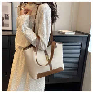 Detail of canvas tote bag showing cream fabric with brown leather trim and gold twist lock