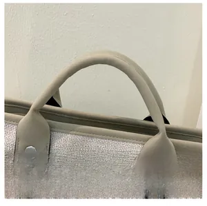 Détail d'un sac seau tissé beige avec poignées en cuir kaki et accessoires en chaîne argentée
