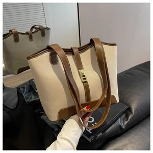 Detail of canvas tote bag showing brown leather trim and golden square buckle lock
