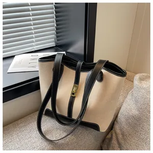 Close-up of canvas bucket bag with black leather trim and golden metal lock on sofa