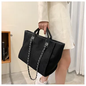 Sac fourre-tout en toile noire avec poignées en cuir et bandoulière chaîne porté par mannequin